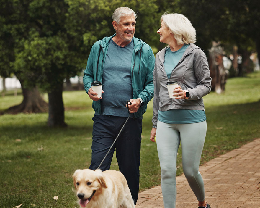 Photo of a man and woman drinking coffee and walking a dog outdoors