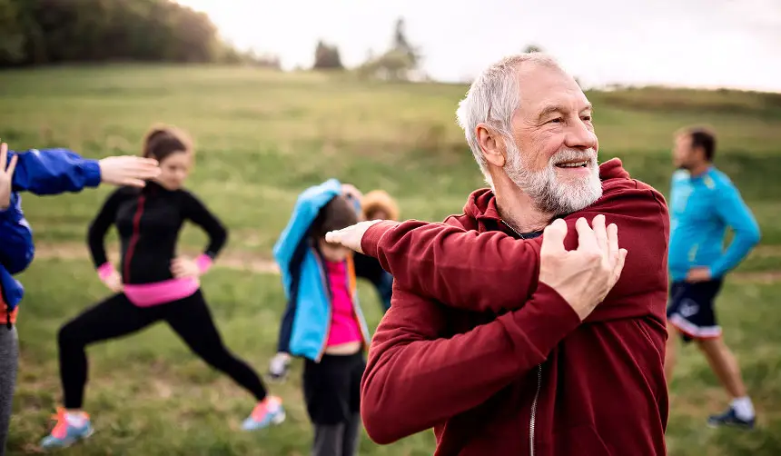 Photo of a man stretching outdoors with other people stretching in the background